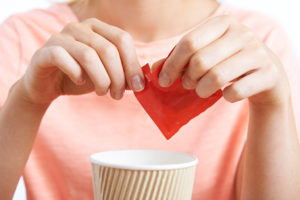 A person puts a red packet of artificial sweetener into their drink.