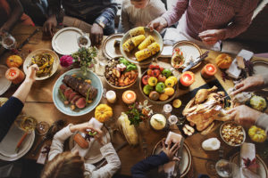Friends and family gather at a table for a Thanksgiving dinner. Plant-based whole foods fill the table. 