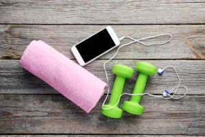 A phone, headphones, green dumbbell weights and a pink workout towel are shown.