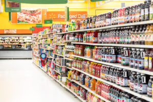 Manufactured foods are in focus in a grocery aisle.