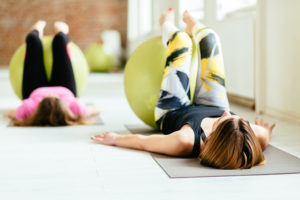 Two women undergo pelvic floor exercises using an exercise ball.