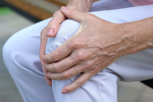 A person clenches their knee with both of their hands.