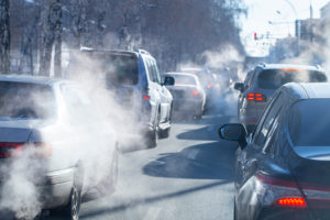 A group of cars are shown with car exhaust covering the street.
