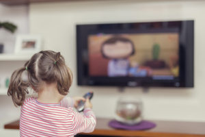 A young girl points a remote at the TV.