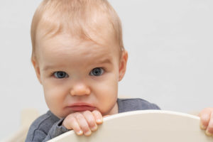 A baby sits in a feeding chair and looks confused.