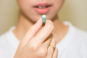 A teenager holds a green pill and prepares to take it.