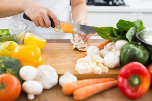 A person uses a knife to cut a wide variety of vegetables on a cutting board.