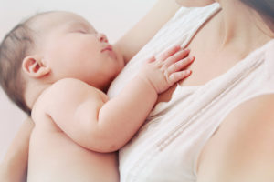 A woman holds her newborn baby close to her chest.  The baby appears asleep.