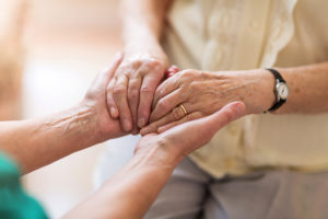 An elderly adult holds hands with someone else.