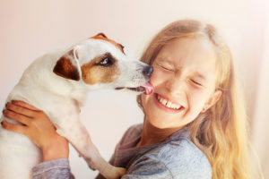 A young girl smiles bigs as she gets a kiss from a dog.