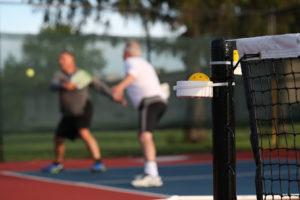 Two adults play pickleball outside.