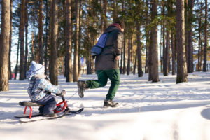 A person pulls a child on a sled outside in the snow.