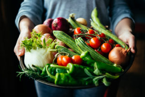 An adult holds out a large bowl filled with vegetables.