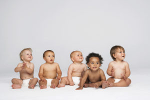 Five babies are sitting next to each other, lined up in a row.