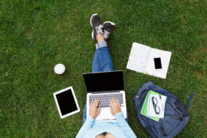 A college student sits outside and works on their homework via their laptop.