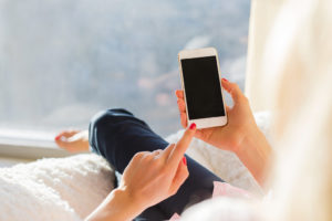 A person holds their smartphone in their hand while they sit on a couch.