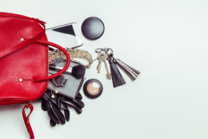 A red purse is shown with keys, makeup, small objects and a phone falling out of it.