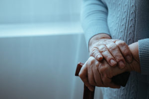 An elderly adult stands by a window, with their frail hands in focus.