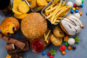 A pile of junk food is placed on a counter.  The food includes: a hamburger, french fires, donuts, chocolate candies and more.