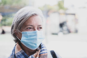 A person wears a medical mask as they stand outside.