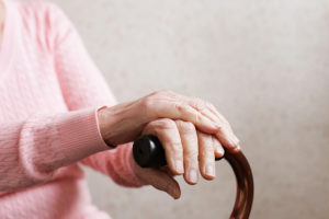 An elderly woman holds onto her cane while she sits inside.