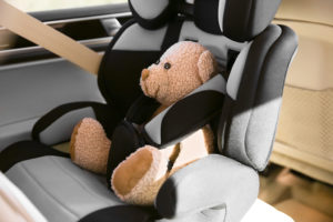A teddy bear sits in a car seat.