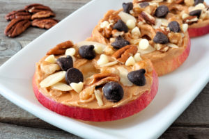 A low-calorie, nutritious snack that fills you up is shown. It is an apple with nut butter and a sprinkling of dark chocolate. 