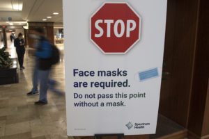 A Spectrum Health sign is posted on a door that reads: "Face masks are required. Do not pass this point without a mask."