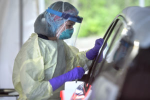 A medical professional wearing a medical mask, face shield and more talks to a patient at a drive-thru COVID testing site.