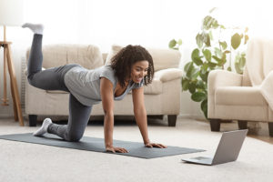 A person exercises at home with a YouTube video shown on her laptop.