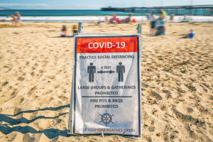 A COVID-19 warning sign is posted at the beach.