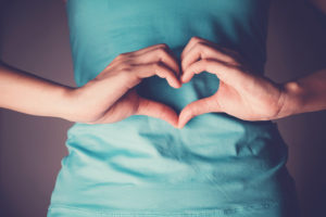 A person shapes their hands into a heart over their gut.