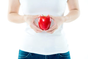 A person holds an apple in front of their stomach.