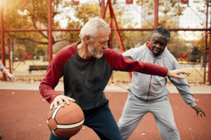 Two elderly adults play street basketball together.