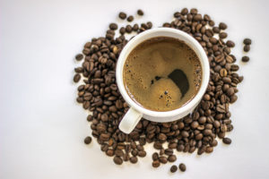 A cup of coffee is surrounded by coffee beans.