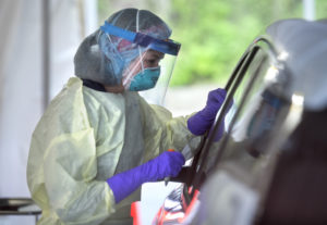 A medical professional wears a mask, gown, gloves and face shield while talking to patients at a drive-through COVID test site.