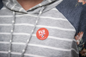 A person wears a “FLU vaccine” sticker.