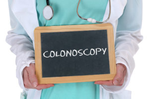 A medical professional holds a sign that reads, “Colonoscopy”