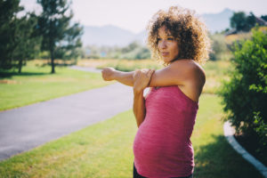 A pregnant woman stretches before she undergoes moderate exercise outside.